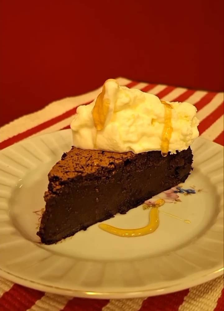 Fatia de bolo melequento com uma montanha de chantilly, sobre toalha listrada de vermelho e branco.