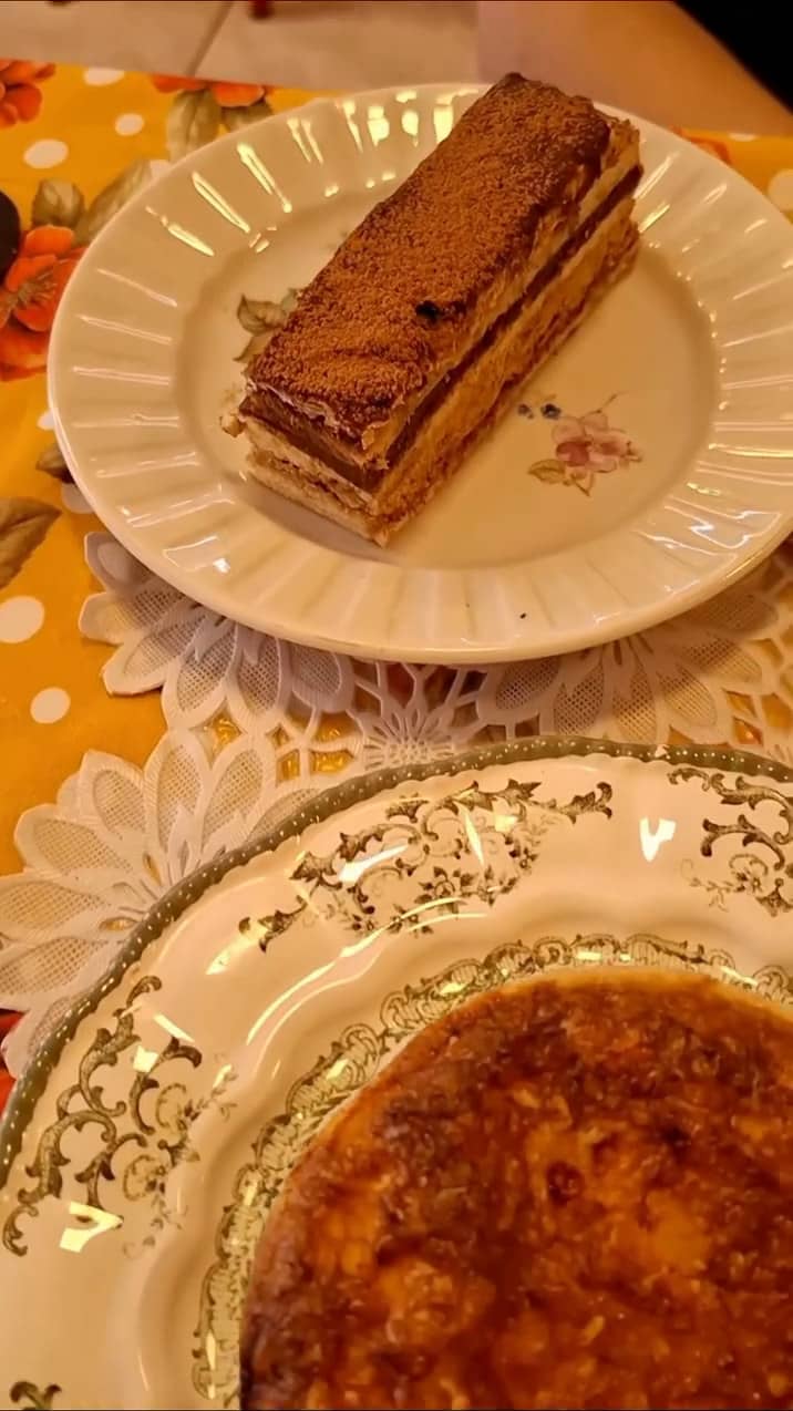Fatia de torta Ópera e uma quiche em pratos antigos sobre toalha de renda e tecido florido.