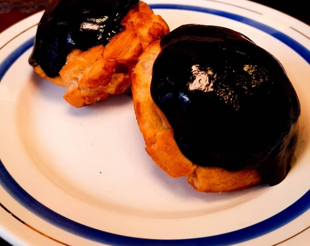 Dois choux cobertos de chocolate brilhante num prato branco de friso azul.