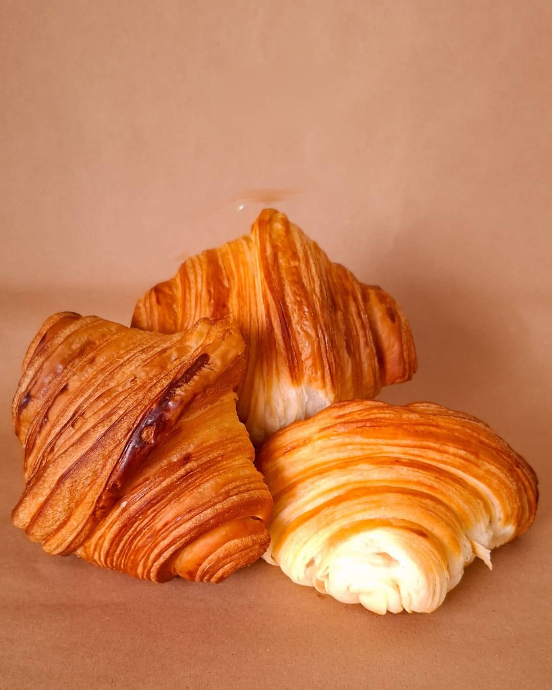Três croissants dourados sobre papel kraft, com as camadas da massa bem marcadas.