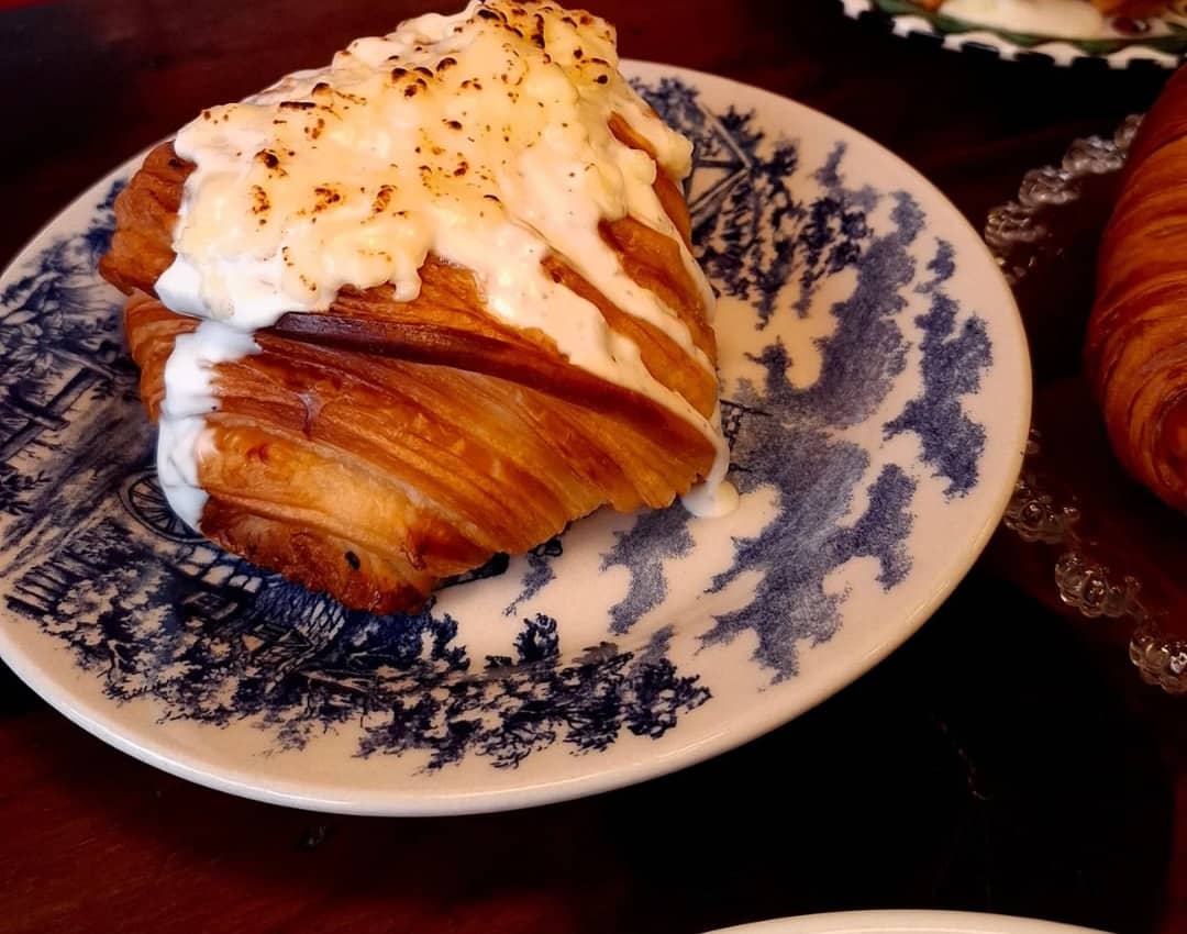 Croissant coberto de molho branco gratinado num prato antigo de louça azul e branca.
