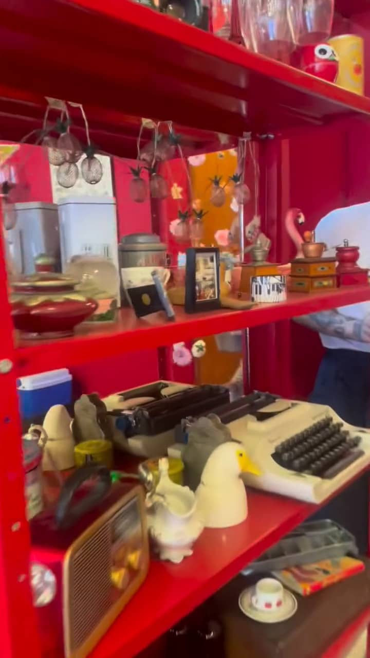 Estante vermelha com máquinas de escrever antigas, rádio, bichinhos de cerâmica e latas.