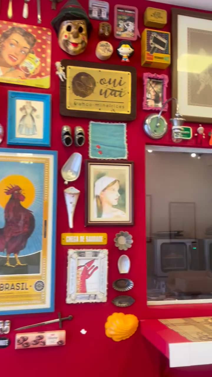 Parede vermelha cheia de quadros e objetos, com uma placa dourada da Oui Uai no meio e a janela da cozinha ao lado.